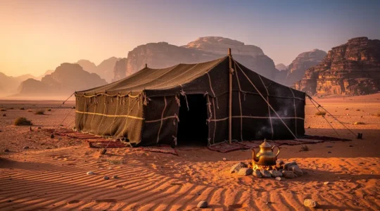 Traditional Bedouin tent in desert landscape with mountains at sunset