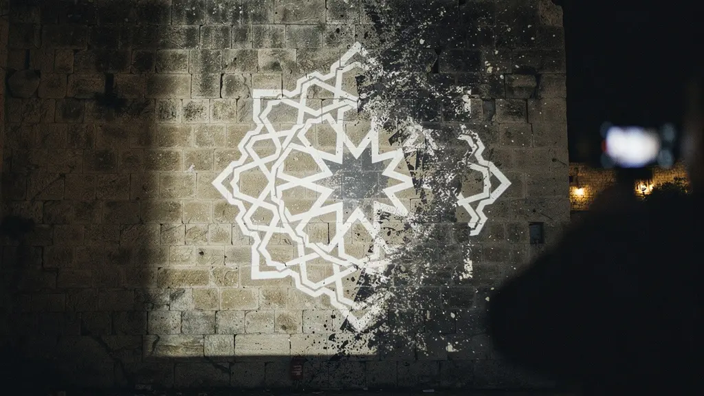 Geometric projection-mapped light patterns appearing to break apart over a heritage stone wall in a dramatic night scene.